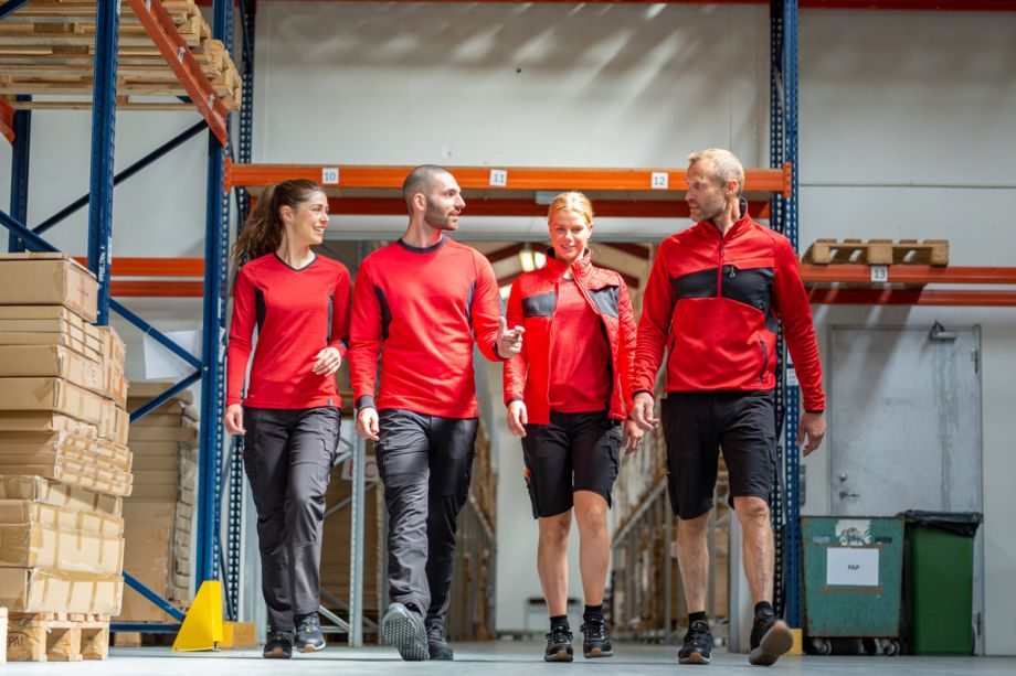 Team in Arbeitskleidung bei einem Rundgang durch das Lager – moderne Berufsbekleidung für Industrie, Logistik und Handwerk.