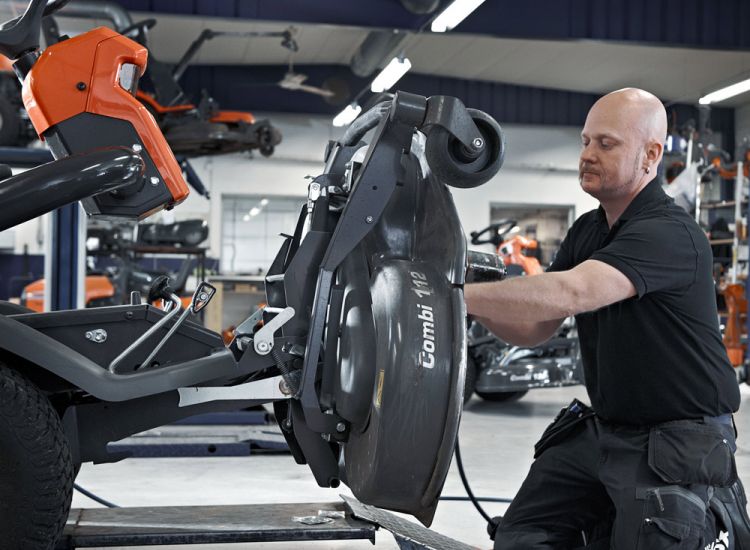 Wartung eines Aufsitzmähers in der Werkstatt – Servicetechniker arbeitet am angehobenen Mähdeck.