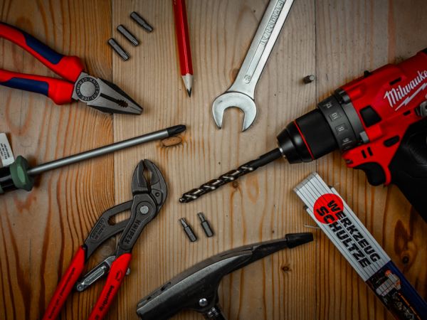 Verschiedene Hand- und Elektrowerkzeuge wie Bohrmaschine, Zangen, Schraubendreher und Schlüssel auf einer Holzoberfläche.